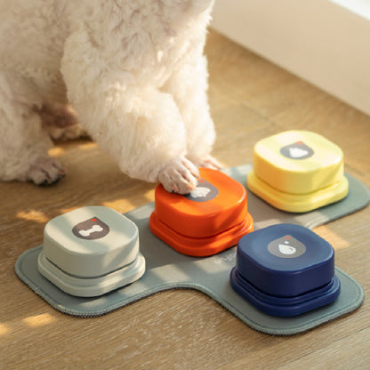 Small white dog pressing orange pet talking button toy set of four colorful buttons on fabric mat