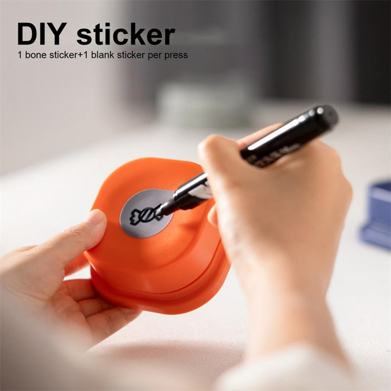 Orange DIY pet talking button toy being customized with a hand drawing a bone sticker using a marker