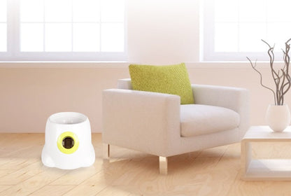 Orange Poppy automatic dog ball launcher white with yellow rim beside armchair on hardwood floor for indoor play