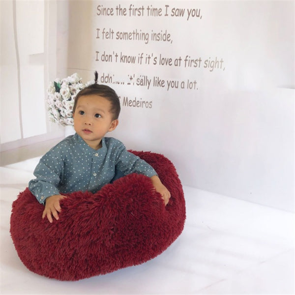Orange Poppy round fluffy cat bed in burgundy red shown with toddler sitting to show size and plush texture