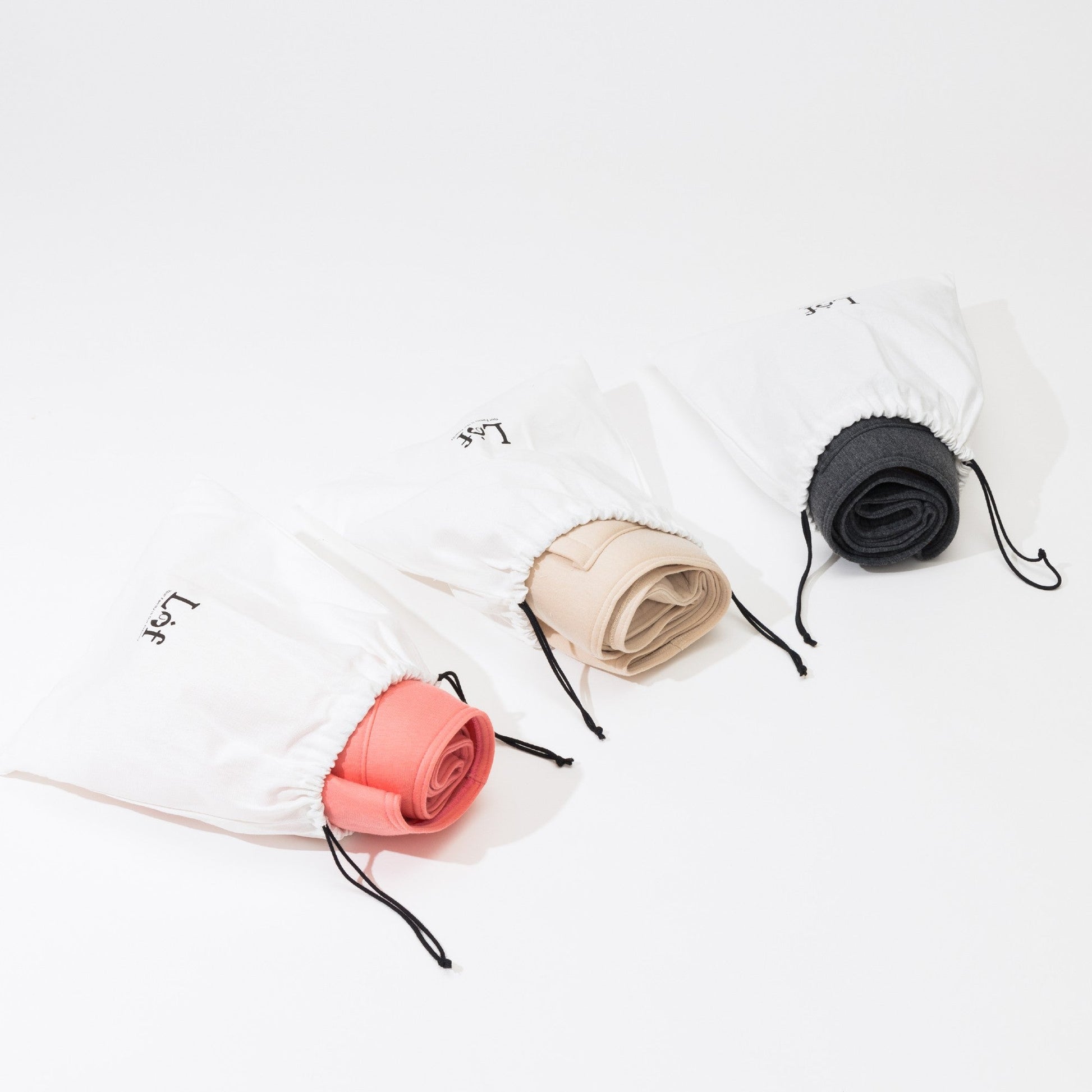 Emerald Alfie pet sling carrier for small dogs rolled up in coral beige and black colors with white drawstring bags