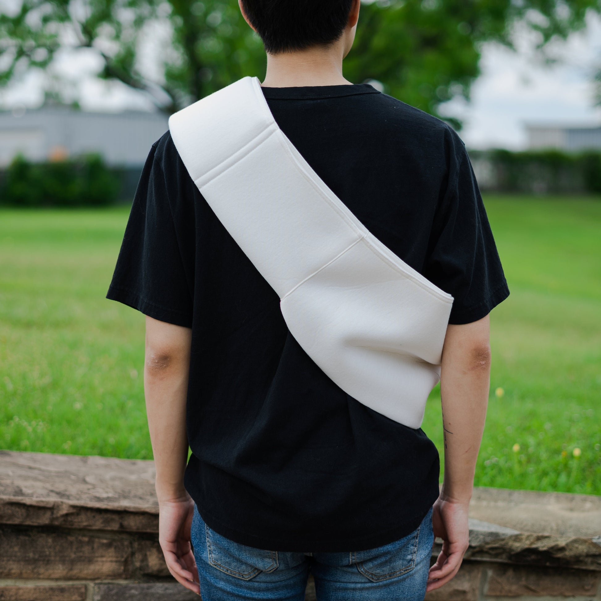 White pet sling carrier for small dogs worn over shoulder by person in black shirt outdoors