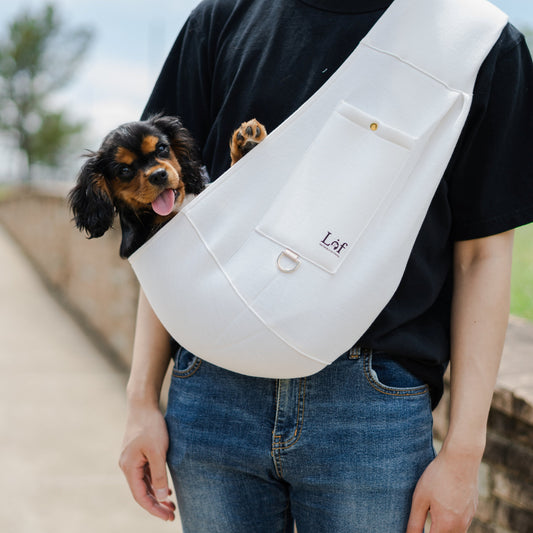 Emerald Alfie pet sling carrier for small dogs in white with a small dog inside worn by a person in black shirt