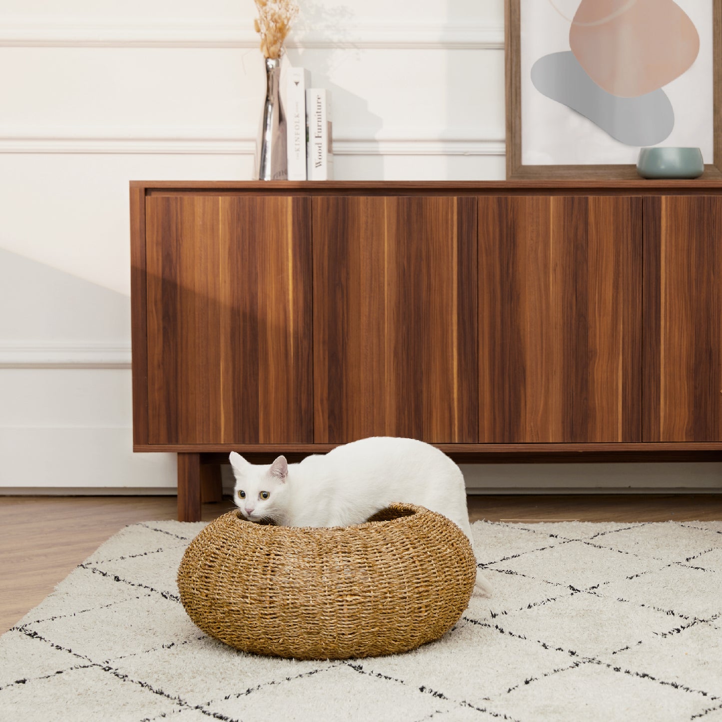 Woven pet bed for cats and dogs by Ochre Menoetius with a white cat resting inside on a patterned rug